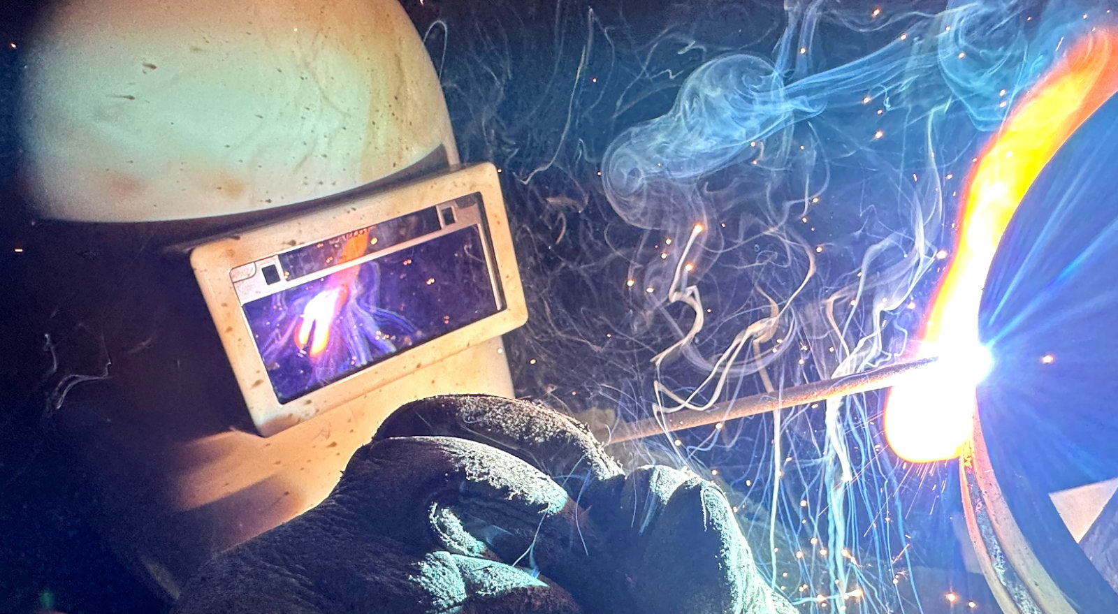 A welder watching a weld closely, with arc light reflecting off lens.